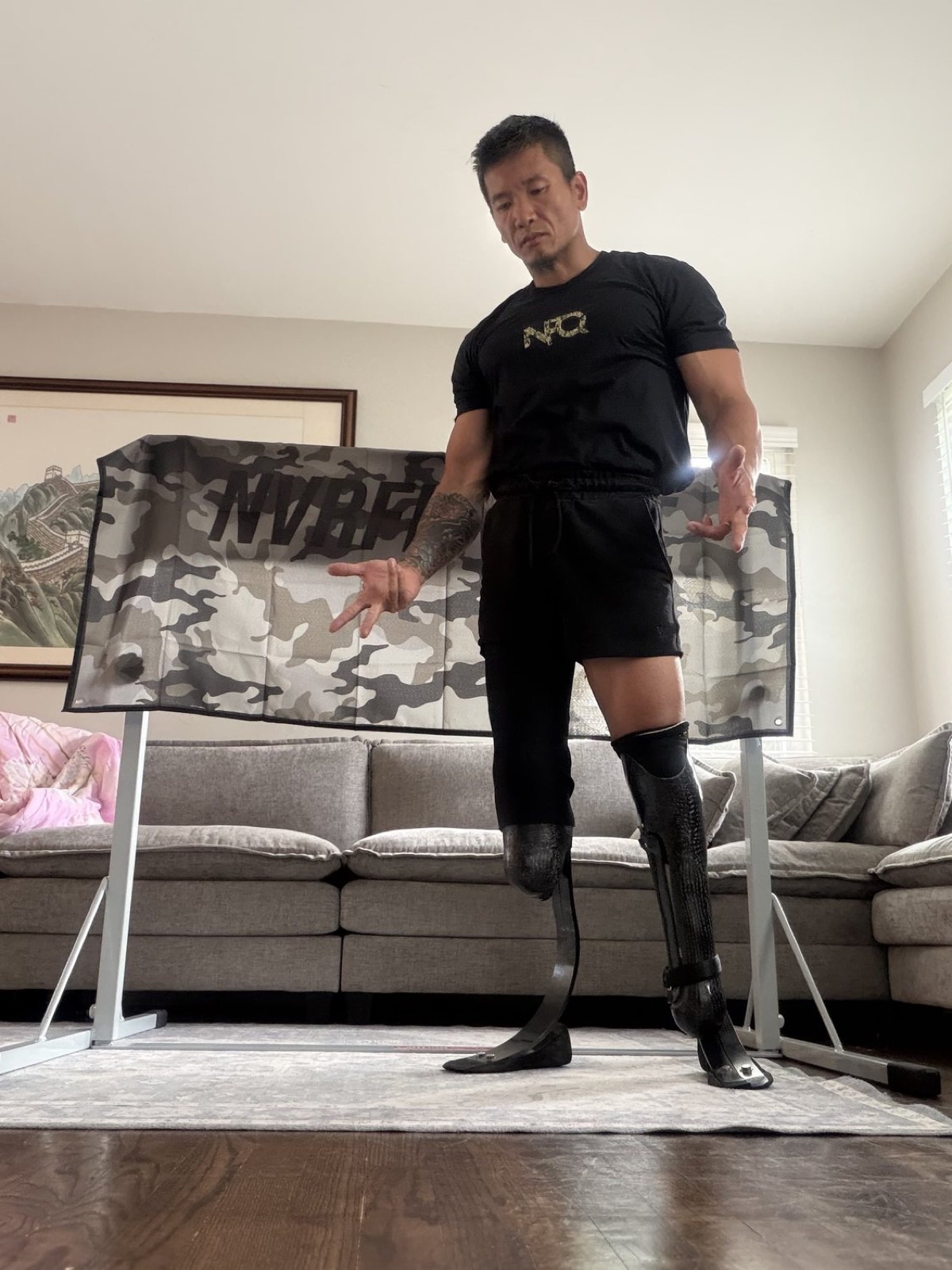Hao Pan standing full-height on his carbon-fiber running blade and prosthetic leg in front of a NVRFKNQUIT banner
