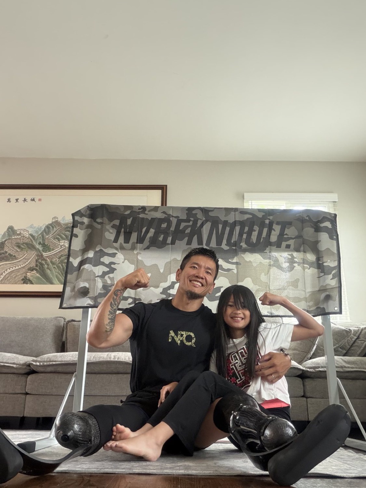 Hao Pan and his daughter flexing together in front of the NVRFKNQUIT banner